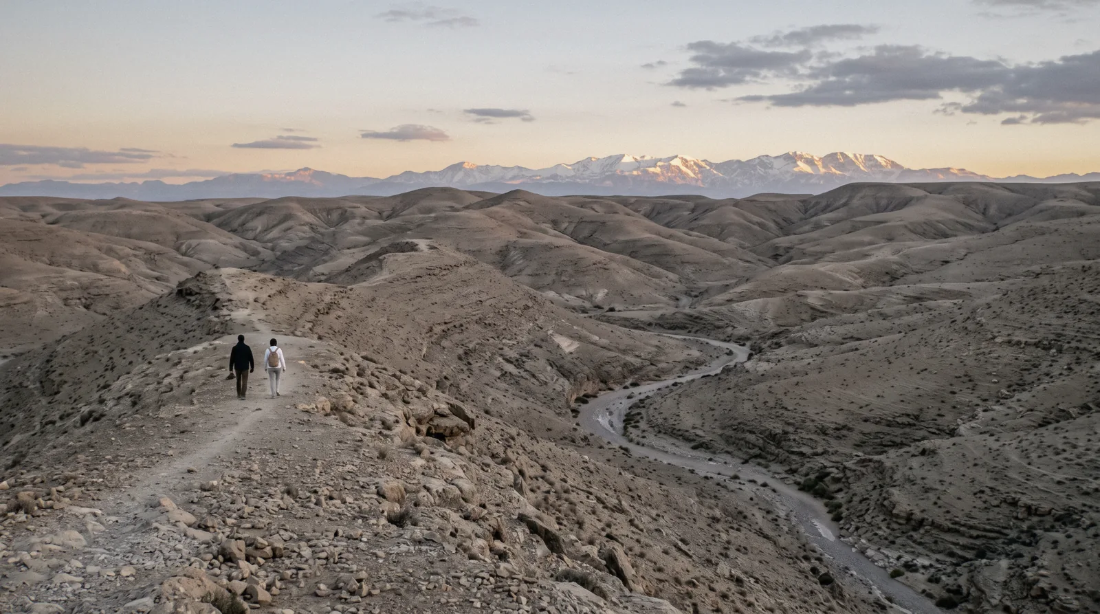 Bare pale hills rolling toward the snow line of the High Atlas at dusk in the Agafay desert outside Marrakech